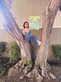 a woman sitting in a tree holding a painting